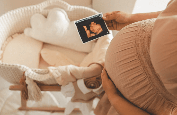 Pregnant woman holding ultrasound near bassinet.
