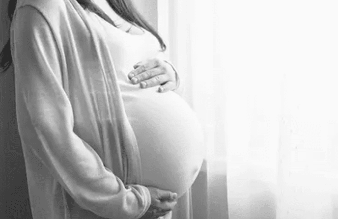 Pregnant woman holding her belly, window background.