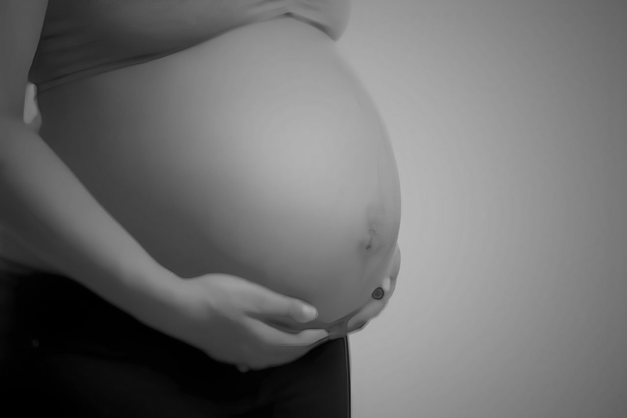 Pregnant woman holding her belly, grayscale image.